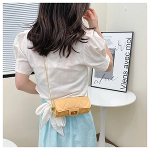 Detail of beige quilted cylindrical bag with golden chain strap on a model outfit