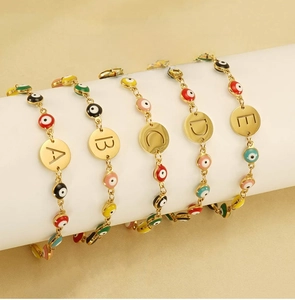 Detailed view of gold stainless steel alphabet evil eye bracelets on white stands