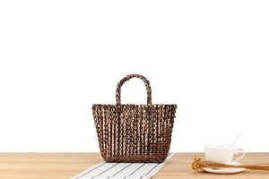 Détail d'un sac cabas marron foncé tissé main avec éclat métallique sur bureau en bois épuré