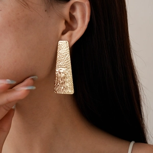 Close-up of geometric gold rectangular earrings with textured metal finish on model