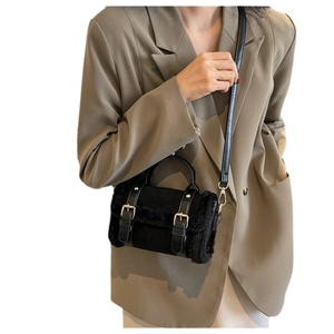 Black plush crossbody bag with leather strap and gold buckle worn by model in beige suit