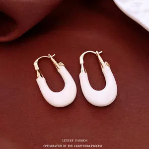 French vintage U-shaped white enamel and gold plated earrings on silk background