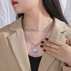Close-up of layered silver necklace with flat snake chain and Virgin Mary coin pendant