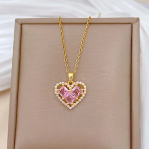 Detailed close-up of a gold heart pendant with pink crystals and pearls on white silk