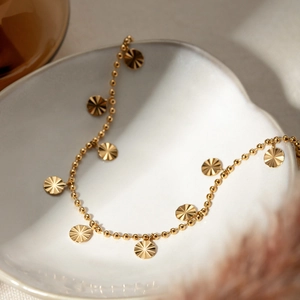 Macro shot of 18K gold stainless steel Cuban anklet with sunburst pattern charms