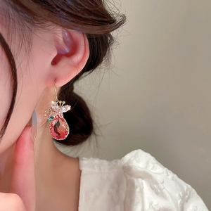Détail de boucle d'oreille goutte rouge avec nœud en zircon doré sur l'oreille