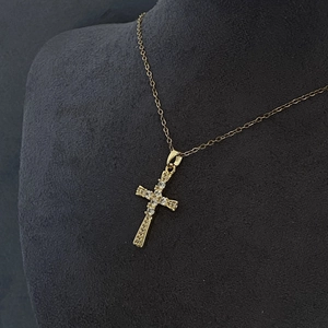 Pendentif croix doré élégant serti de zircons blancs sur un mannequin gris