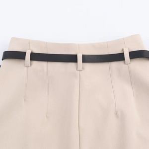 Detailed macro view of the high-waisted beige trousers featuring a sleek black belt