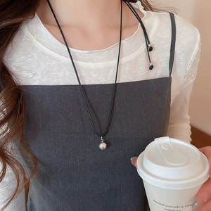 Detail of silver ball pendant on black cord necklace worn by a model for minimalist style