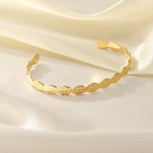 Detail of a gold hammered stainless steel open bangle on white silk background