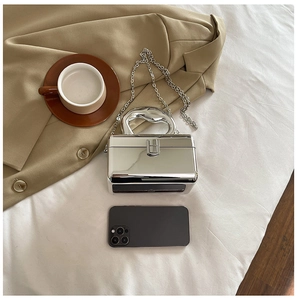 Close-up of a silver mirror acrylic box bag with metal chain on a white sheet backdrop