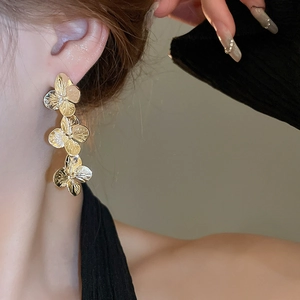 Close-up of gold metallic floral earrings with three connected flowers worn by a model