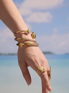 Gros plan de bracelets et bagues plaqués or 18 carats avec zircon 5A sur fond de plage