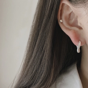 Close-up of minimalist twisted U-shape silver hoop earring and square stud on ear