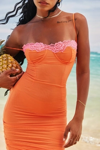 Detail eines orangefarbenen Netz-Minikleides mit rosa Spitzenbesatz am sonnigen Strand