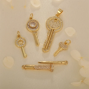 Gold-plated key and nail pendants set with cubic zirconia on elegant beige background