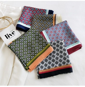 Detail view of colorful geometric floral silk scarves styled with a white shirt and straw bag