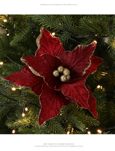 Detail of burgundy velvet Christmas flower with gold glitter edges on a lit Xmas tree
