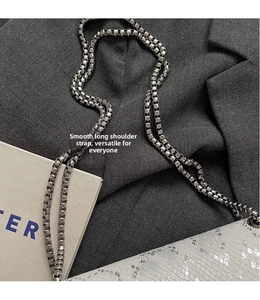 Detail of silver box chain strap on white snakeskin leather bag and grey suit fabric