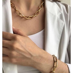 Detail of chunky gold chain link necklace and bracelet set on a white blazer