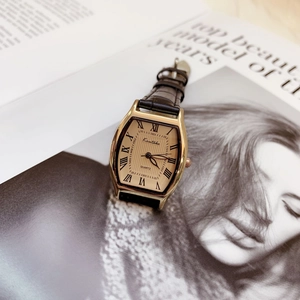 Fashion tonneau quartz watch with gold rectangular dial and black leather strap on a magazine