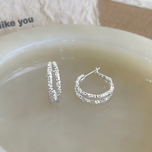 Detailed close-up of silver geometric hoop earrings with textured diamond-cut finish