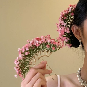 Detailed close-up of a golden flower hair pin with delicate pink baby's breath blossoms