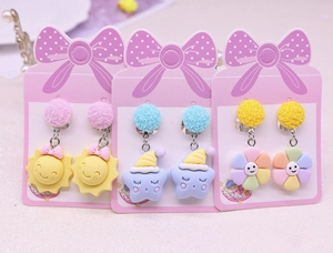 Detailed view of three pairs of children's clip-on earrings with sun, star and flower charms