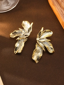 Detailed view of large golden flower earrings with brushed metal texture on brown leather