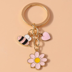 Detail of bee, heart, and daisy flower charms on a golden key ring with enamel finish