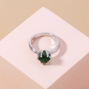 Macro view of a silver ring with a green gemstone on a soft pink geometric display stand
