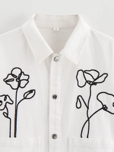 Detail of white cotton shirt with black floral embroidery and metallic buttons