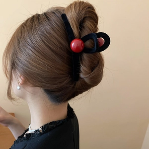 Detail view of a vintage red ball and black velvet hair claw clip on a sleek updo hairstyle