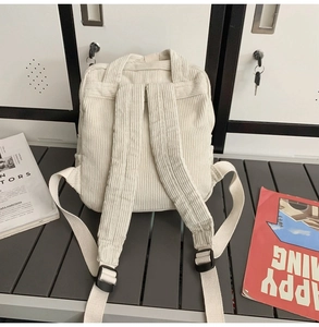 Vue arrière d'un sac à dos beige en velours côtelé avec bretelles rembourrées sur un banc