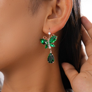 Macro shot of emerald butterfly earrings with teardrop crystal pendant on a model