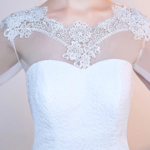 Close-up of white lace wedding dress featuring floral embroidery and mesh neckline
