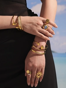 Gros plan sur un ensemble de bracelets et bagues ajourés plaqués or 18 carats sur la plage