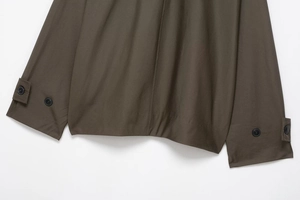 Detail of dark olive trench coat cuff with adjustable strap and black button closure