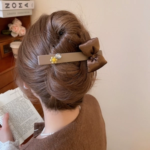 Detail view of a brown satin bow hair clip with diamond flower on elegant bun hairstyle
