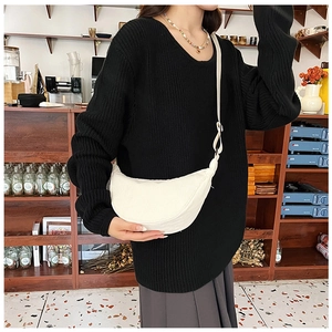 Close-up of white corduroy crescent bag worn over a black sweater in a cafe setting