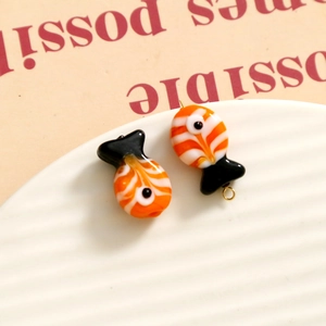 Macro shot of orange and white glass fish charms on a textured white jewelry tray