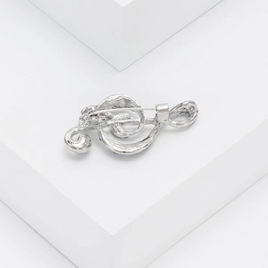 Macro detail of silver treble clef music note brooch pin on minimalist white background
