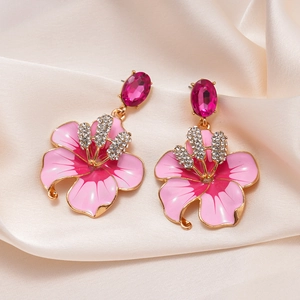 Dettaglio macro di orecchini floreali con petali in smalto rosa e strass lucidi