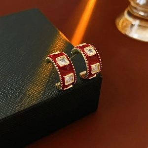 Macro shot of gold-plated red enamel C-shaped earrings with square zircon on a black gift box