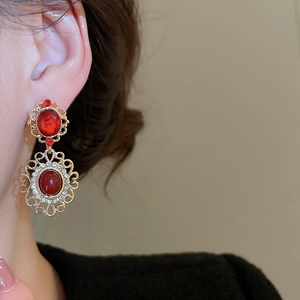 Detail of vintage palace style earrings with red gemstones and gold filigree on a model