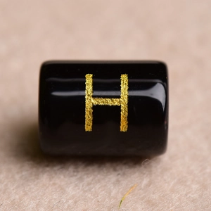 Macro shot of a black cylindrical bead with a gold letter H for DIY jewelry making