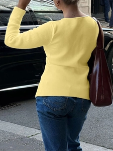 Rear view of a yellow long sleeve knit shirt worn by a model in an urban setting