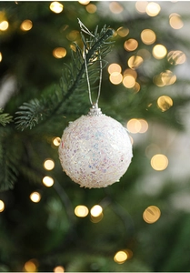 Close-up of a white iridescent glitter Christmas ball hanging on a green tree branch
