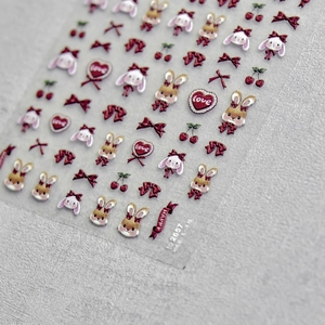 3D embossed nail stickers with cute rabbits, red bows, and hearts on grey textured background