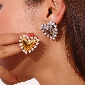 Detailed close-up of heart-shaped gold and silver pearl earrings on a model ear